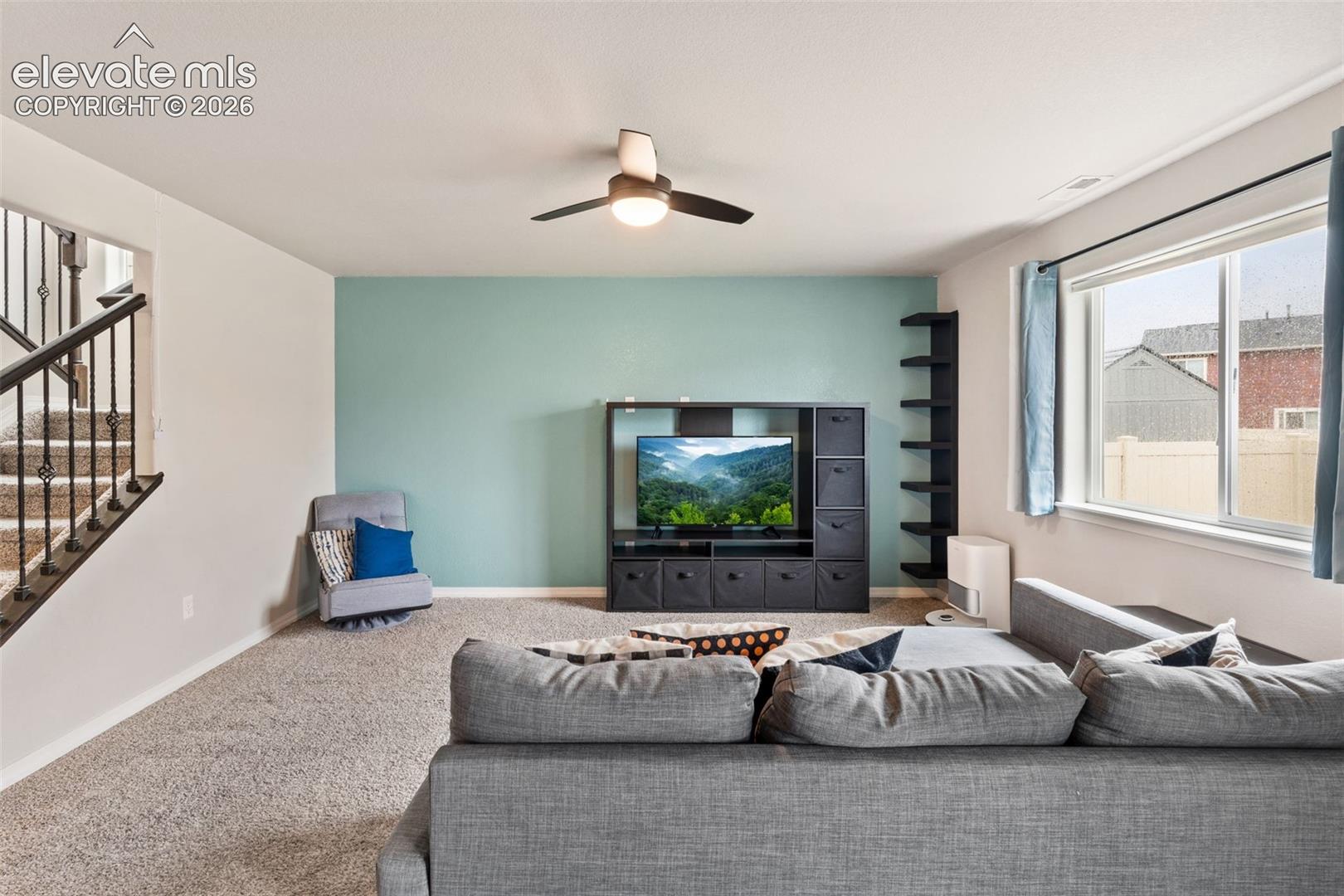 Carpeted room featuring a ceiling fan, a window with blinds, and a built-in shelving unit