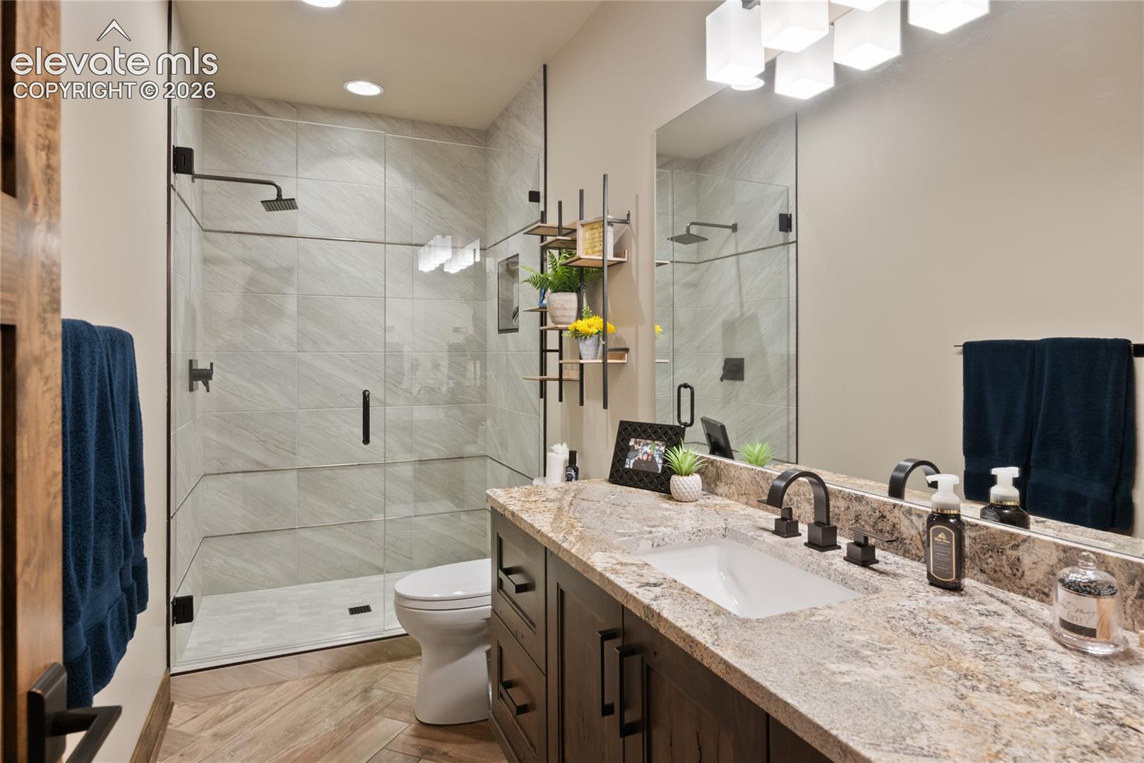 Hall bath that could pass for an ensuite. Large walk-in shower with full tile surround, custom granite vanity, designer fixtures, and herringbone tile floors.