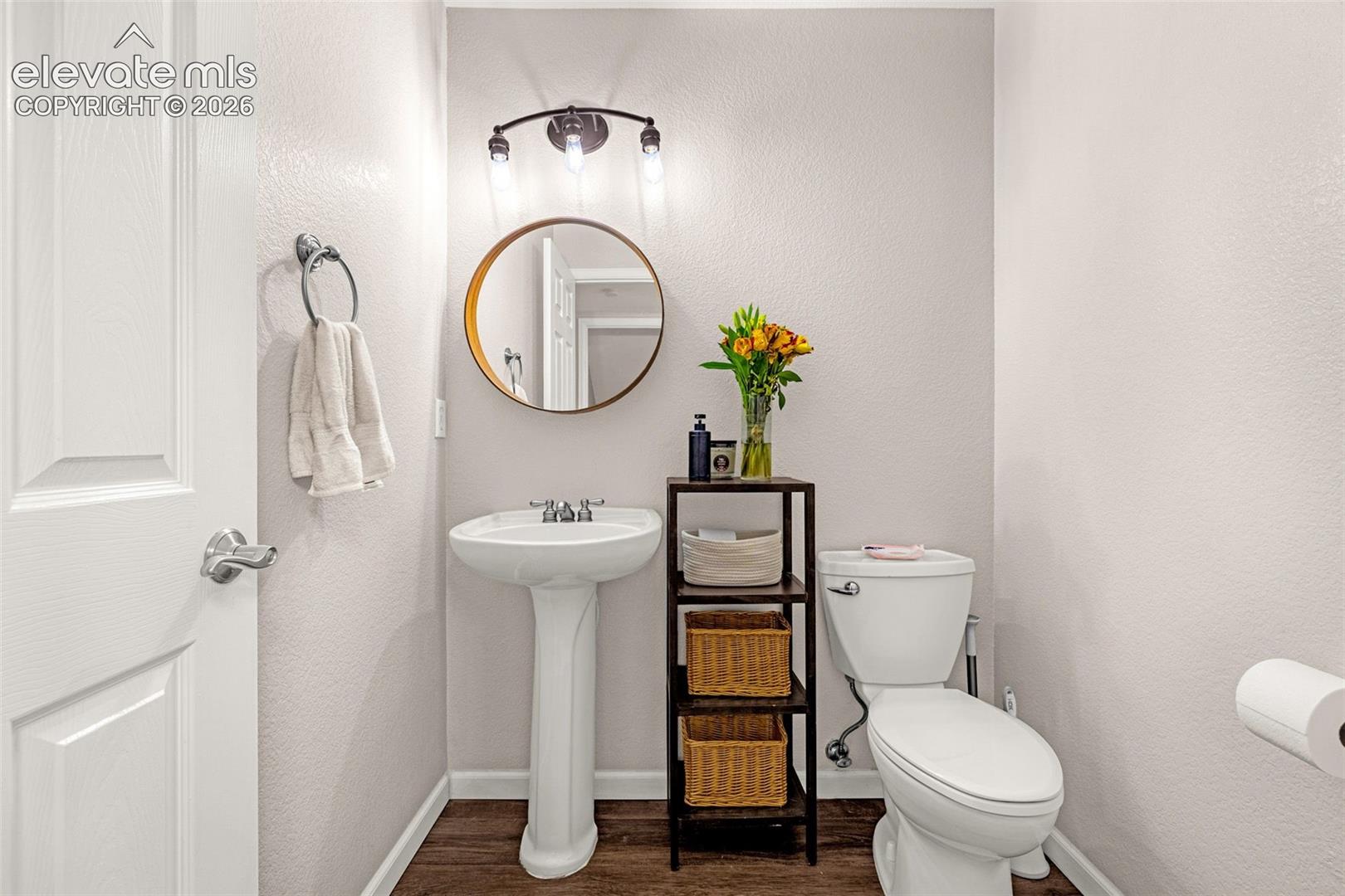 Pedestal sink with polished chrome widespread faucet, round wall-mounted mirror, three-light fixture with glass shades, and wood-finish flooring