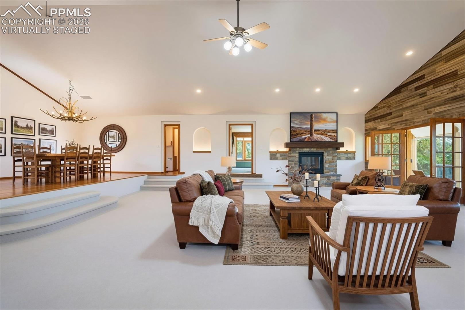 virtually staged Vaulted ceiling living area featuring a stone fireplace with wood mantel, wood accent wall, and recessed lighting
