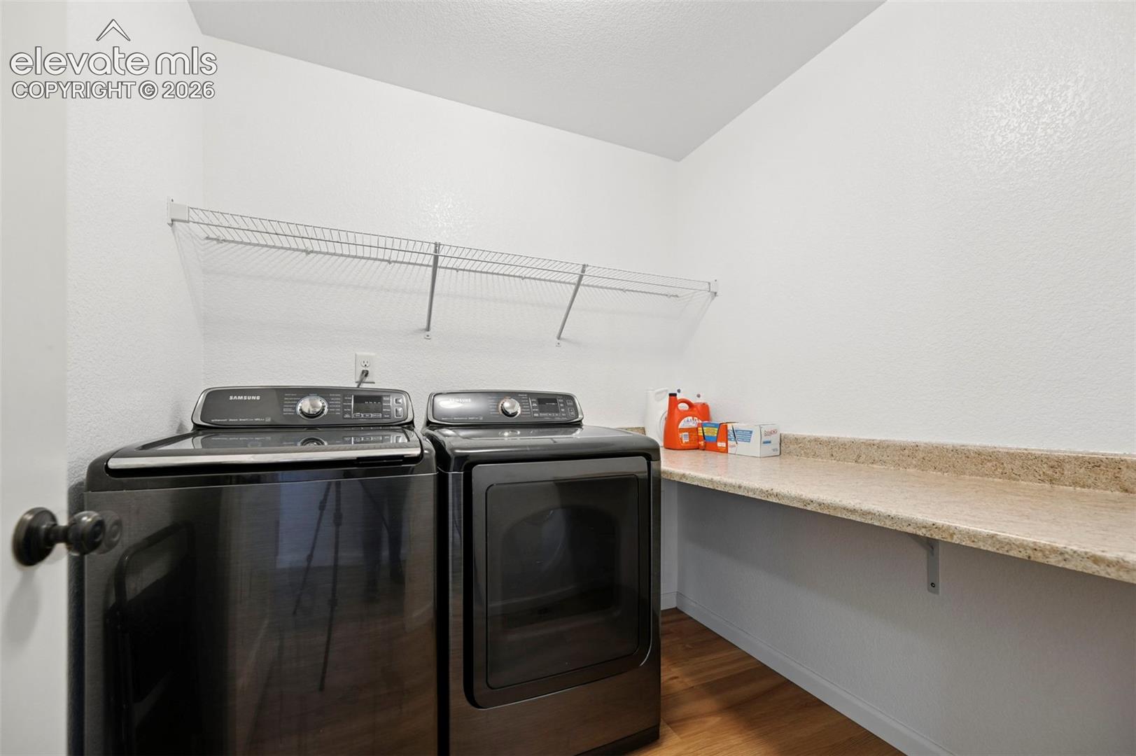 Laundry area featuring stone-surface countertop, wire shelving, and wood-finish flooring