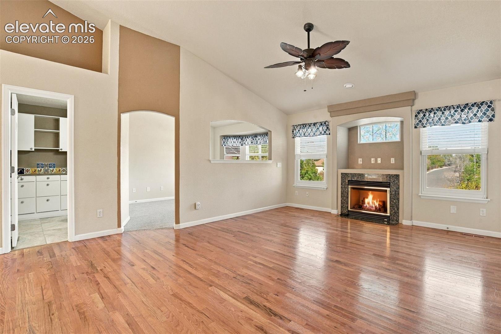 Vaulted ceilings featuring a built-in ceiling fan, wood-finish flooring, and a fireplace with a stone-finish surround