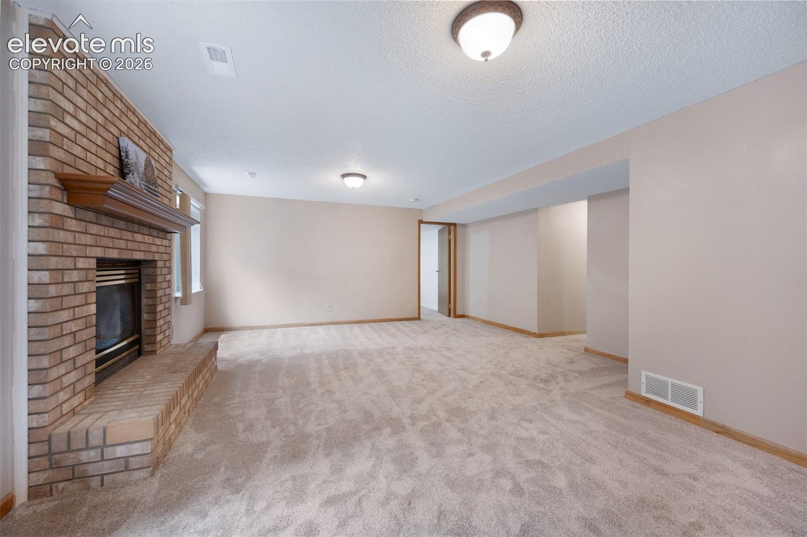 Unfurnished living room featuring a fireplace, carpet, baseboards, and a textured ceiling