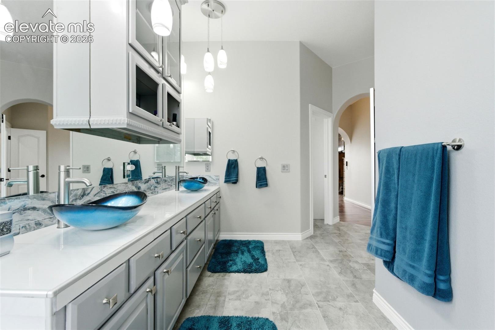 Dual vessel sinks, expansive vanity with extensive cabinetry, overhead storage, and pendant lighting