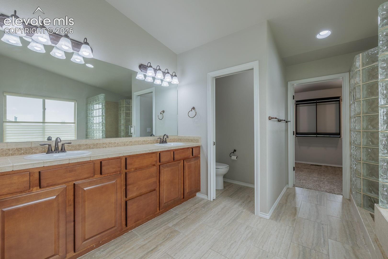 Spa-inspired primary bathroom featuring a wood-finish vanity with dual sinks, quartz countertops, and polished chrome fixtures and double fireplace