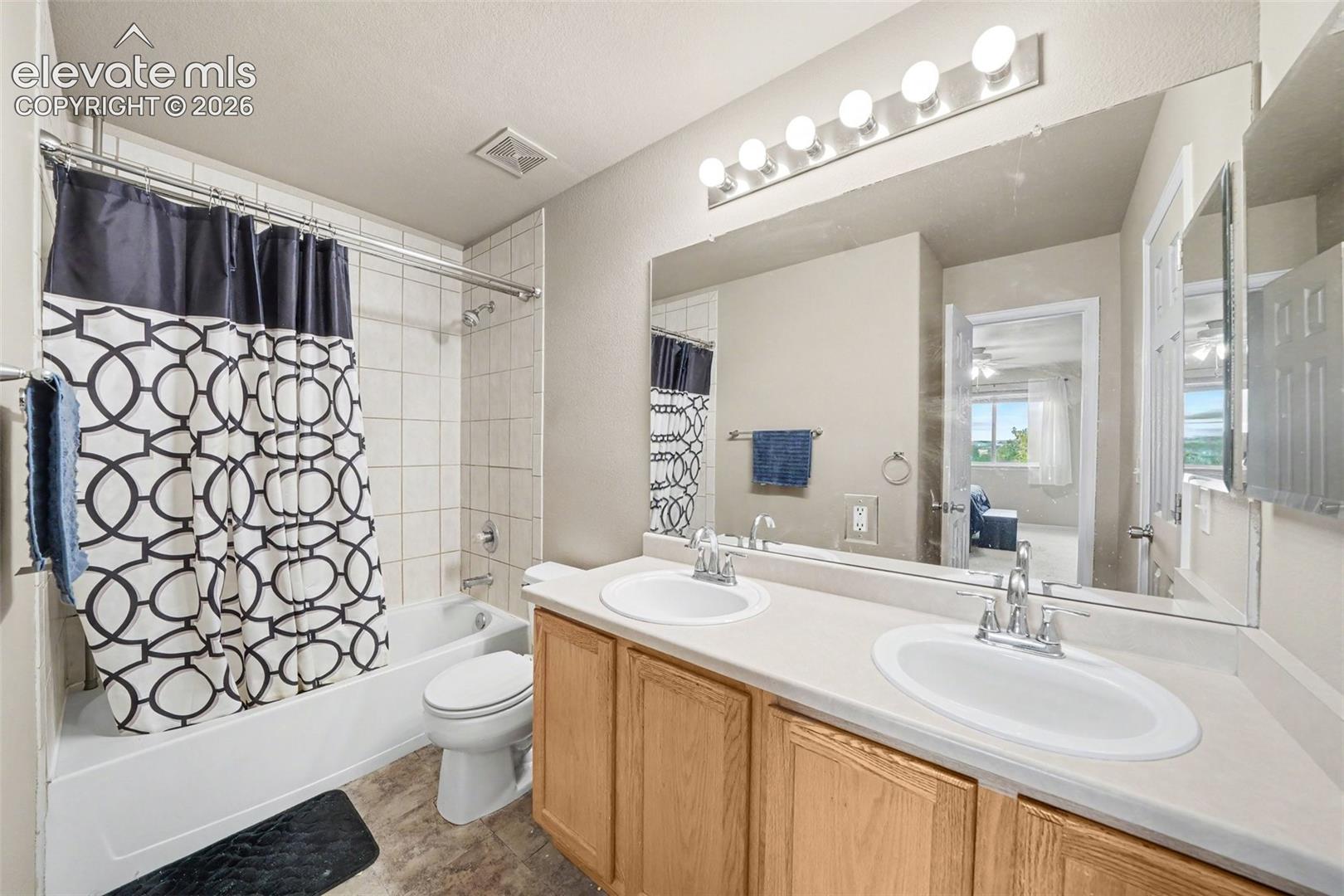 Double vanity with integrated sinks, wood-finish cabinetry, full-width vanity mirror, six-light fixture, and tub-shower combination with tile surround