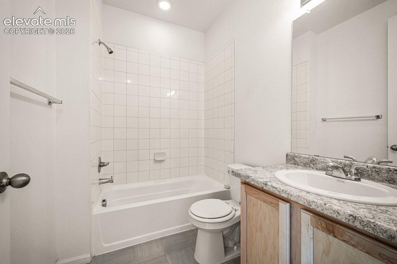 Bathroom featuring a tub/shower combination with white subway tile surround, wood-finish vanity with a light-toned countertop, and recessed lighting