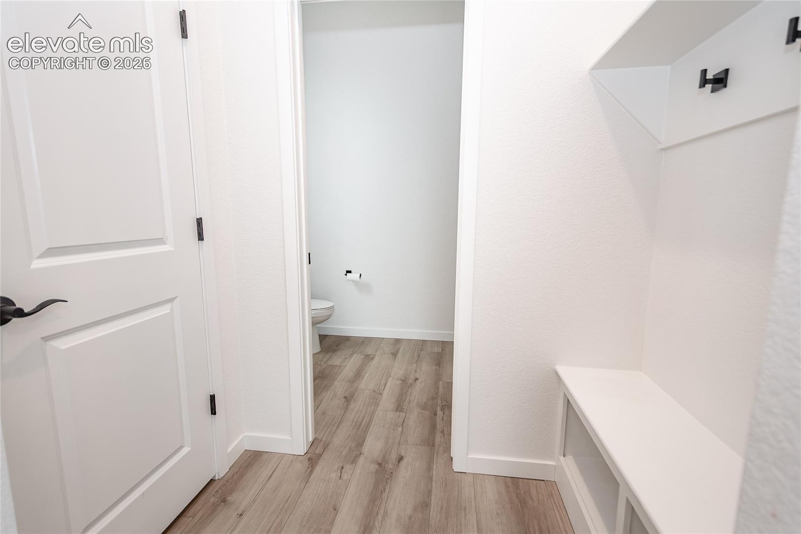 Built-in white mudroom bench featuring integrated shelving and matte black hardware, wood-finish flooring, and solid-core door with matte black lever handle