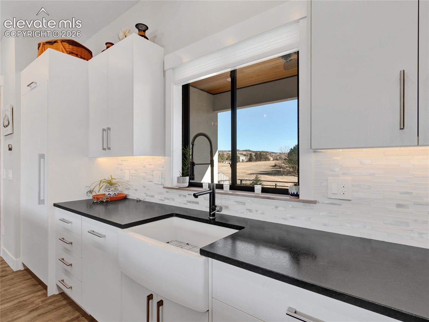 Modern kitchen featuring white cabinetry, dark countertops, a white farmhouse-style sink with a matte black faucet, under-cabinet lighting, and a white subway tile backsplash
