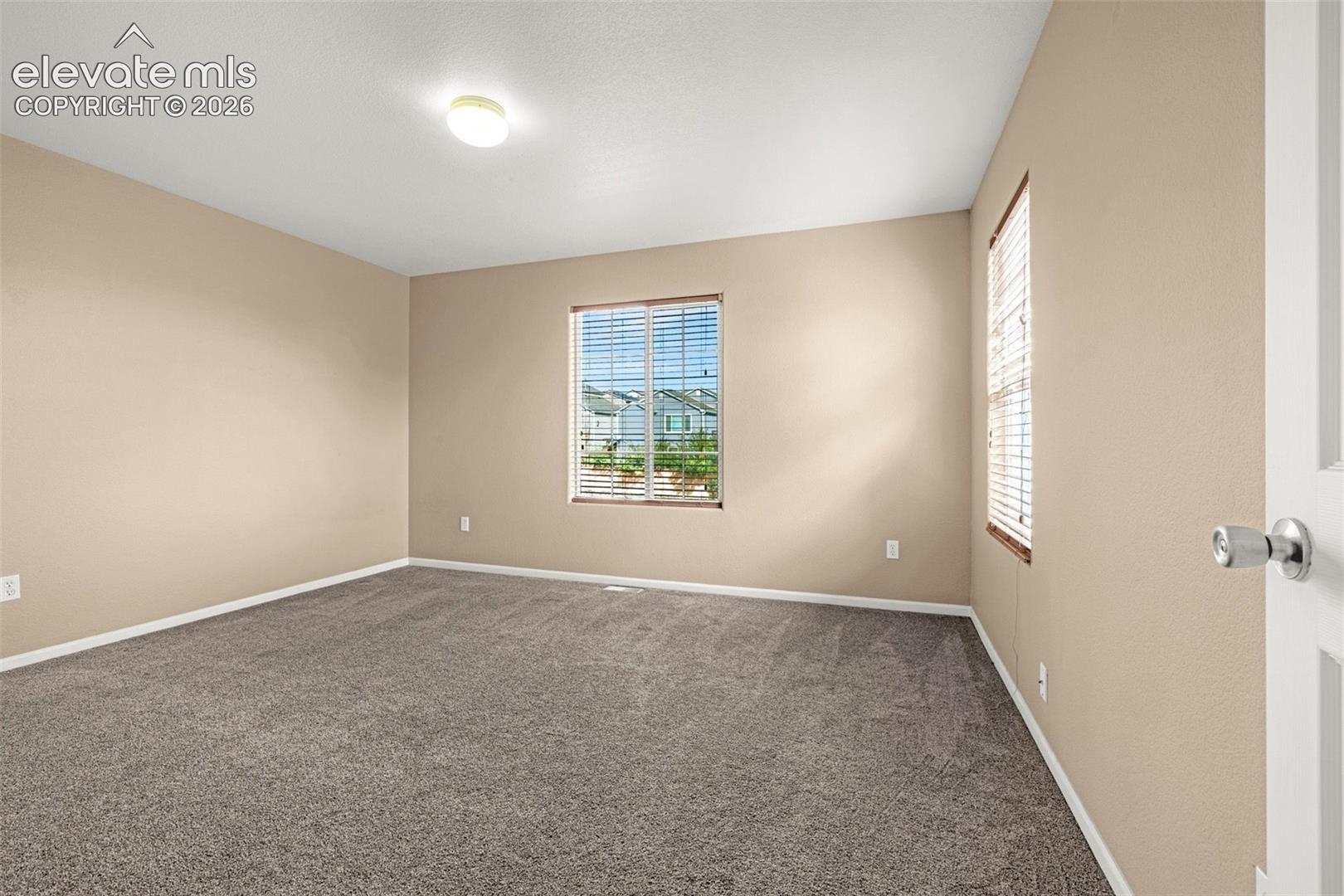 Recessed lighting, neutral wall tones, two windows with blinds, and durable carpeting