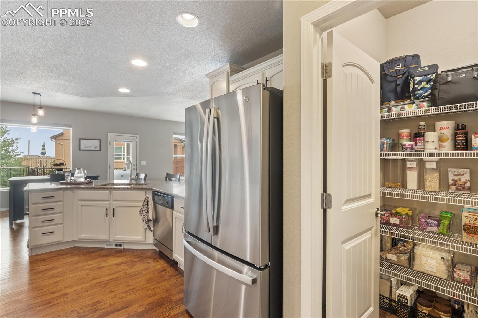 Kitchen with stainless steel appliances, a peninsula, a textured ceiling, white cabinetry, and light wood-type flooring
