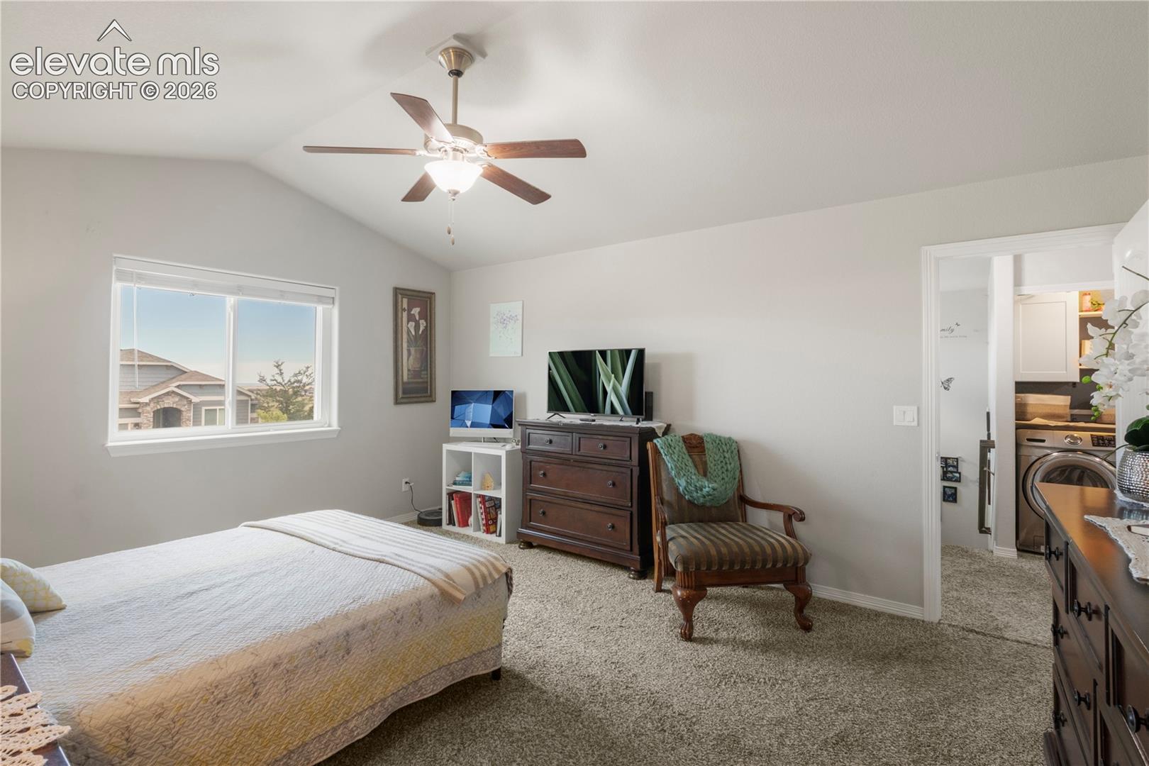 Vaulted ceiling with a ceiling fan, carpeted flooring, and a large window