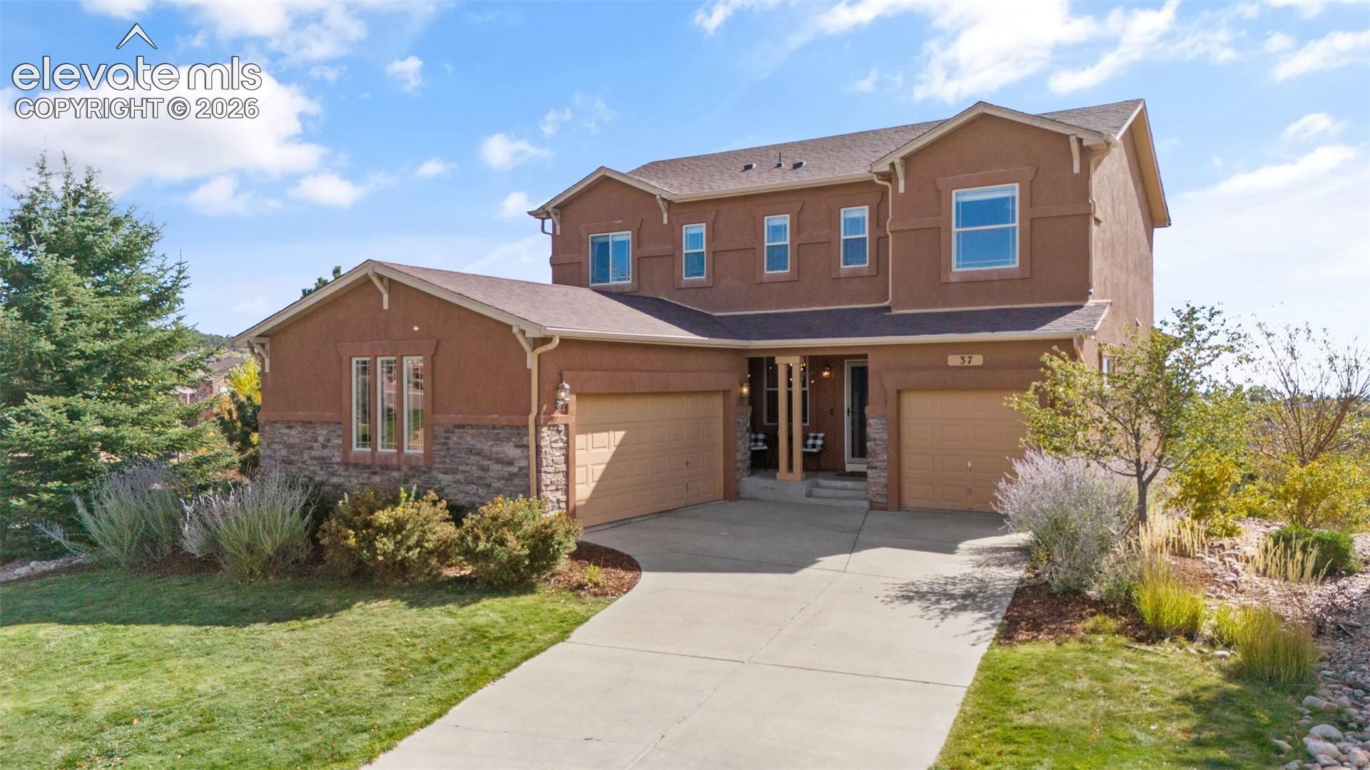 Two-story residence featuring a stucco exterior with stone veneer accents, an attached three-car garage, and a concrete driveway