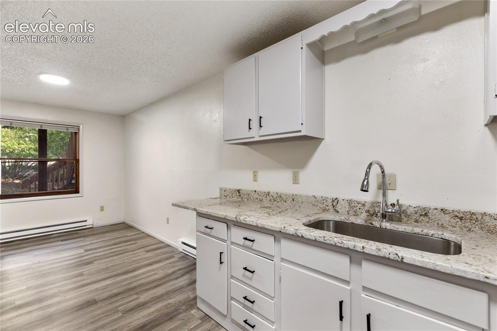 Compact kitchenette featuring white cabinetry, a speckled countertop, and a stainless steel sink with a gooseneck faucet