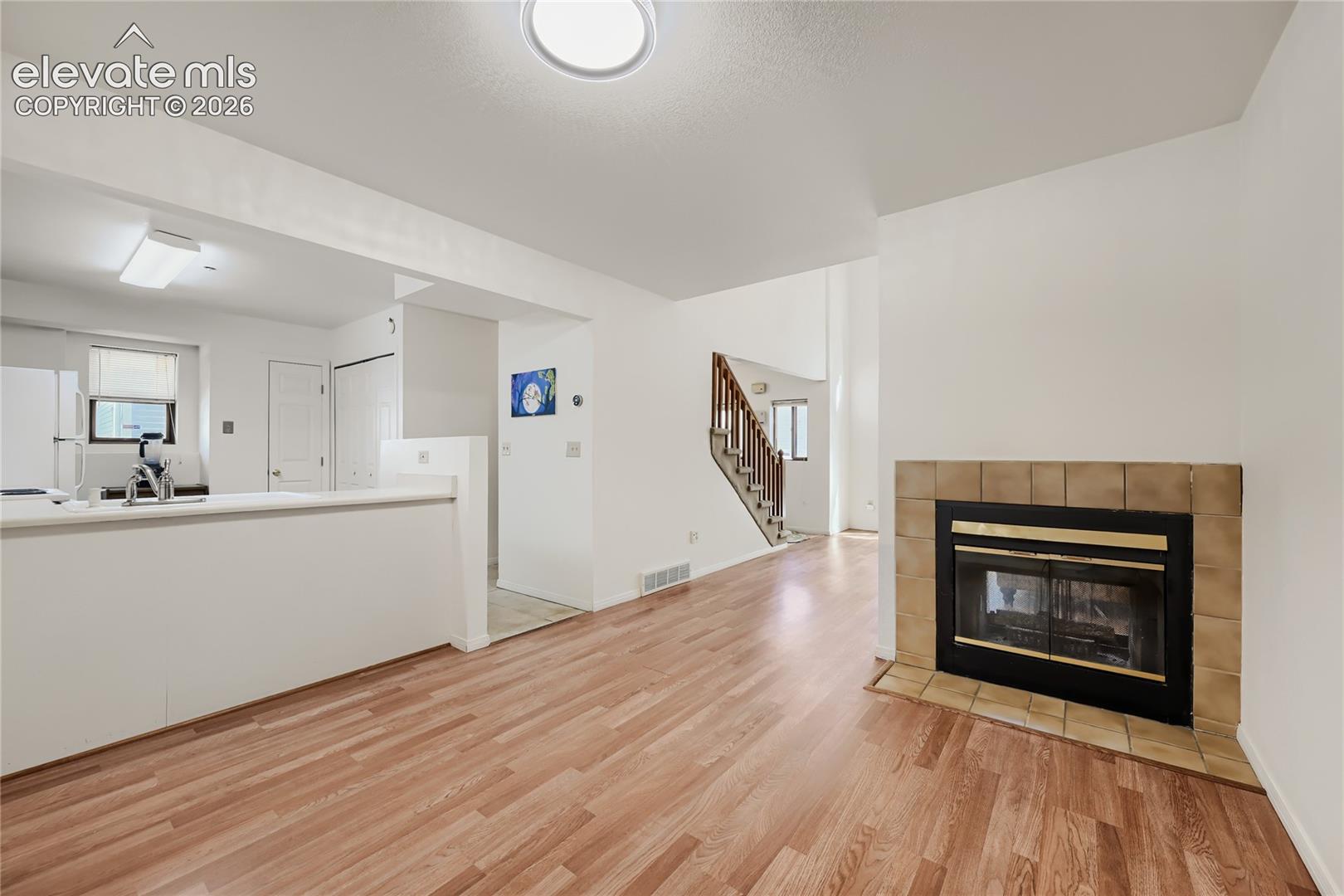 Wood-finish flooring throughout, featuring a tiled fireplace with hearth, and an open-concept kitchen with white appliances and a stainless steel faucet