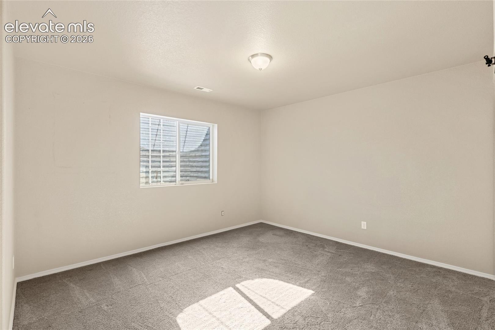 Neutral-toned interior space featuring wall-to-wall carpeting, a single window, and a centered flush-mount ceiling light fixture