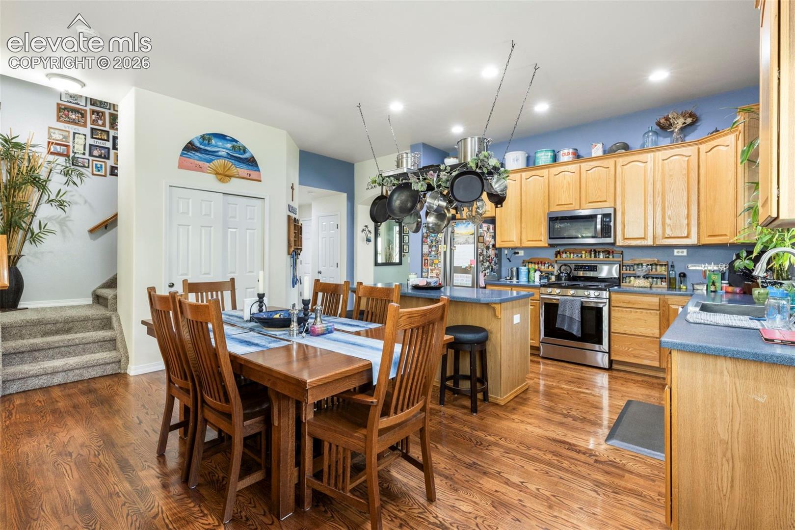 Kitchen and dining area featuring wood-finish flooring, light wood cabinetry, stainless steel appliances, and a central island with bar seating