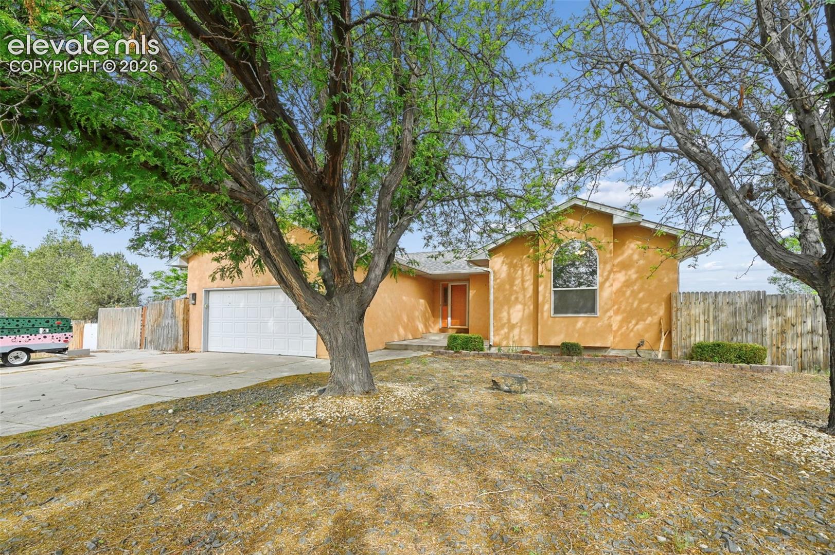 Saffron stucco exterior featuring an arched window, a two-car garage, and a wood privacy fence