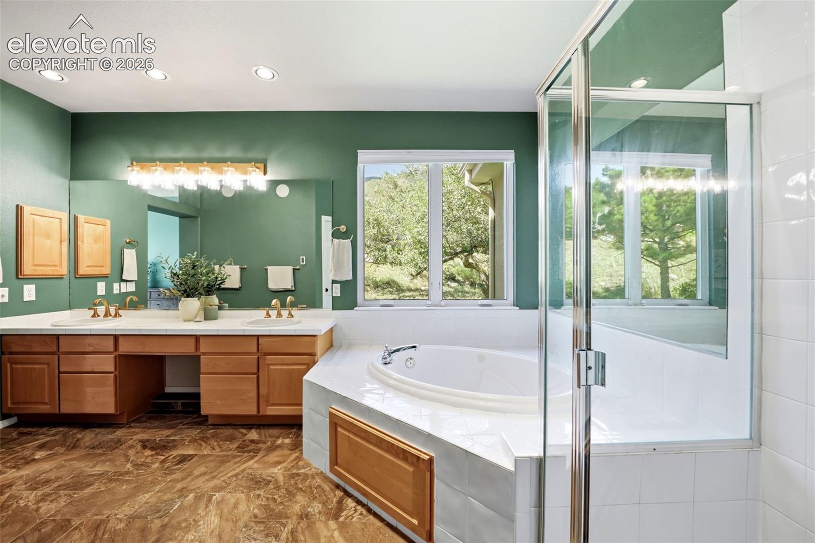 Dual vanity with extensive countertop space, wood-finish cabinetry, and an integrated jetted tub