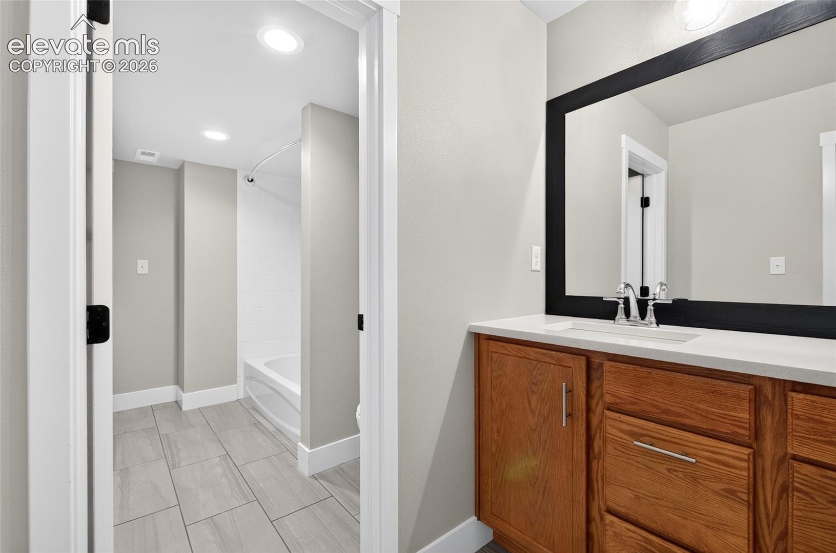Shared with main floor bedroom and library, Bathroom vanity featuring a quartz countertop, integrated sink, and wood-finish cabinetry with brushed nickel hardware