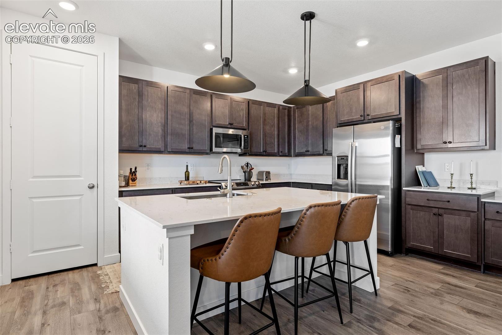 Kitchen featuring LVP flooring, dark wood cabinetry, stainless steel appliances, a center island with a light-colored countertop, and recessed lighting