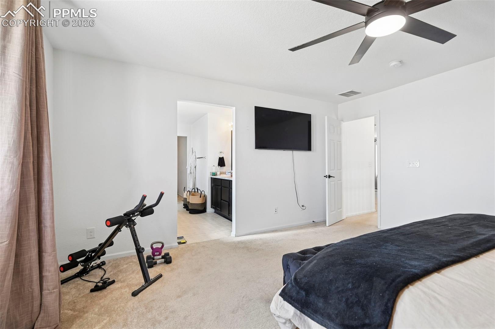 Carpeted bedroom with a ceiling fan and mounted television