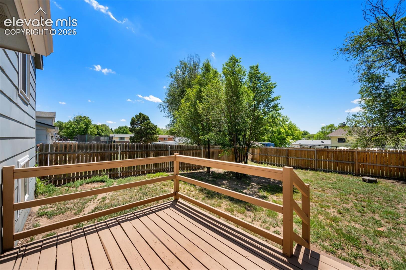 Expansive composite deck with wood-finish railings and multi-level design overlooking a spacious fenced yard with mature landscaping and established trees