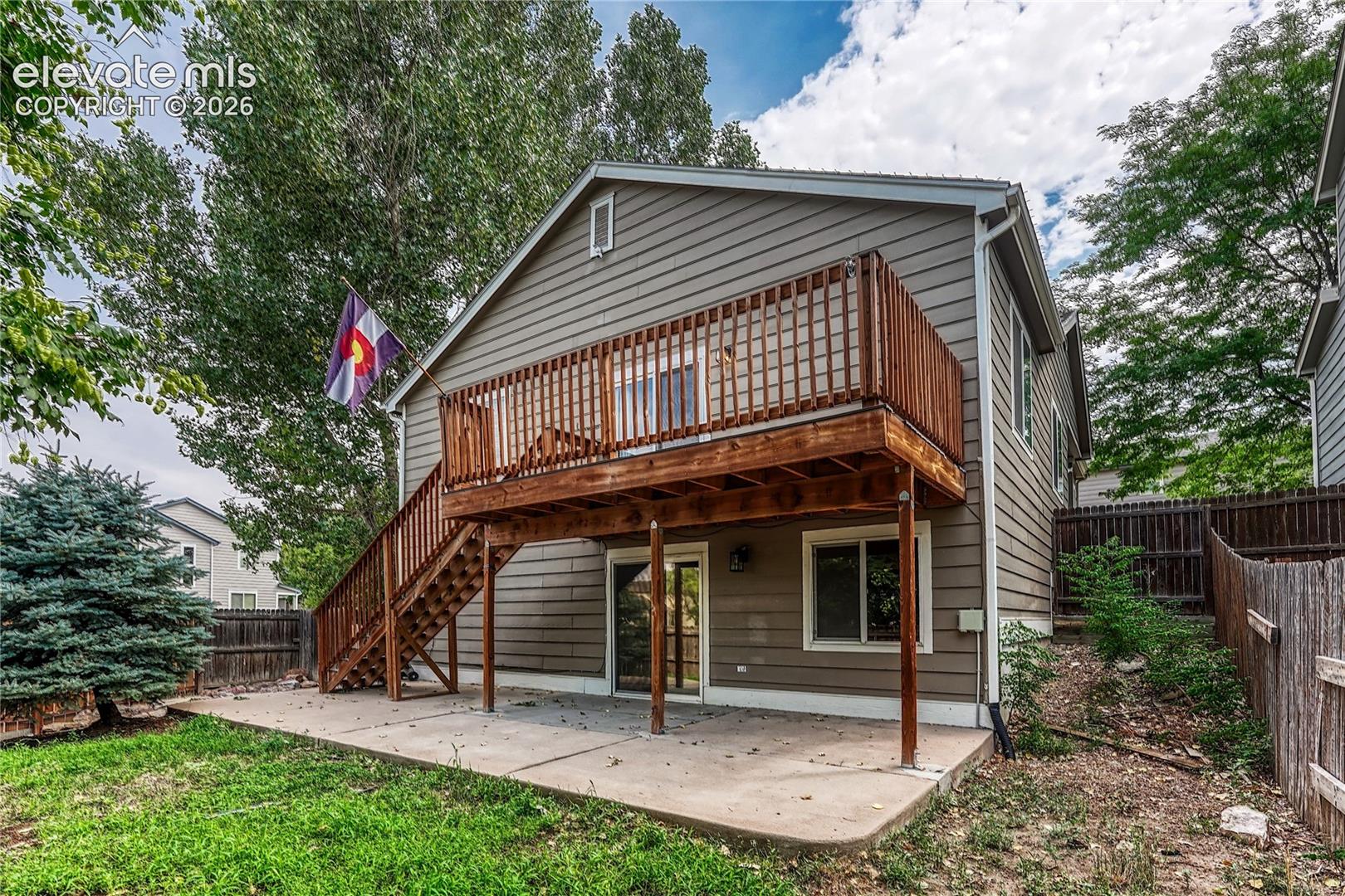 Exterior elevation featuring horizontal lap siding, elevated wood deck with railing, staircase, ground-level concrete patio, and sliding glass doors