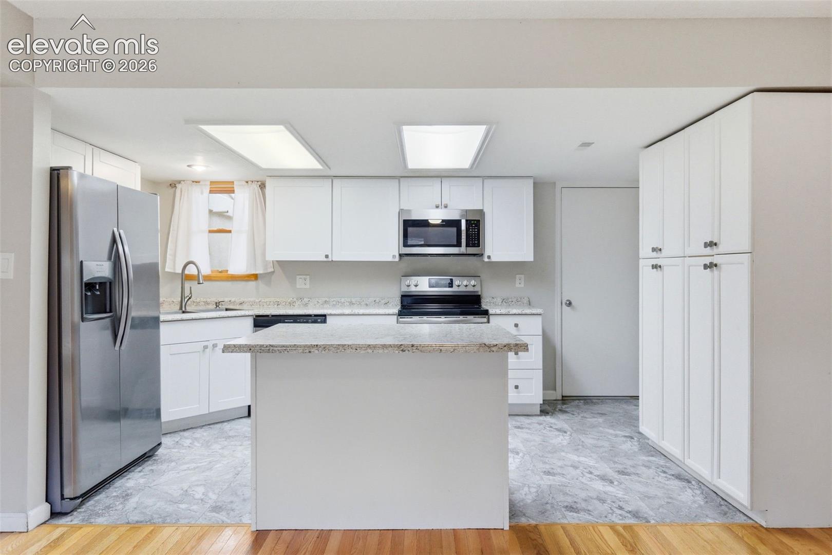 Kitchen featuring white cabinetry, stainless steel appliances, a center island with countertop, and marble-look flooring
