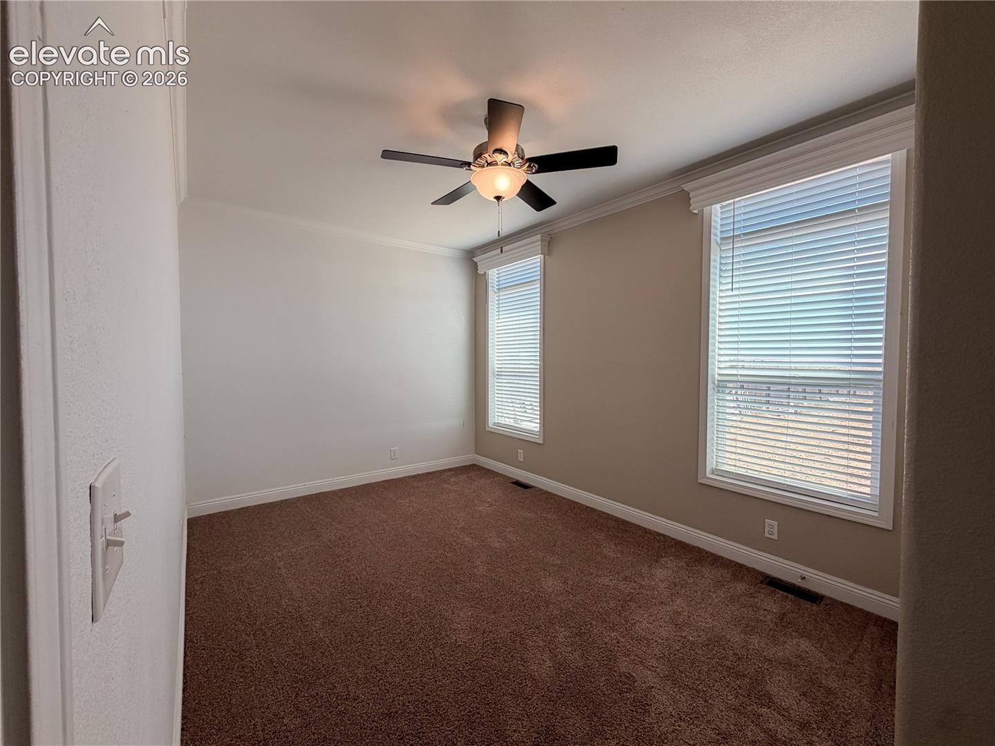 Interior room featuring neutral wall paint, crown molding, wall-to-wall carpeting, two windows with horizontal blinds, and a central ceiling fan with integrated lighting