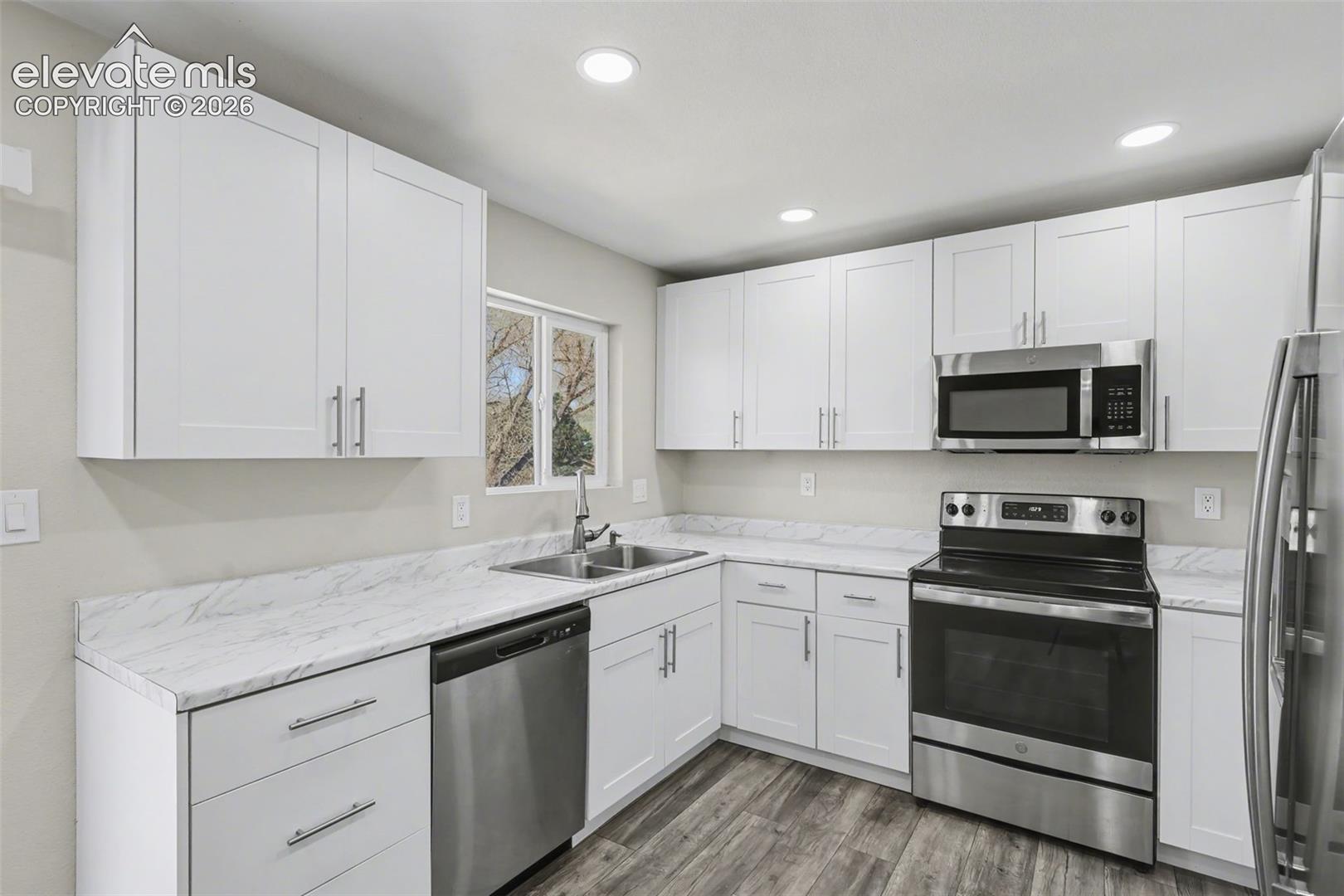 Kitchen featuring white shaker-style cabinetry, stone-patterned laminate countertops, stainless steel appliances, recessed lighting, and wood-finish flooring