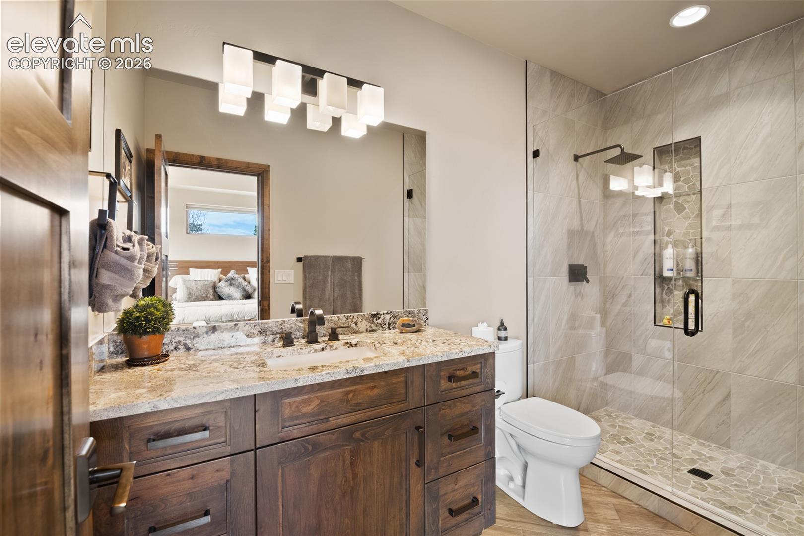 Private ensuite featuring a full granite vanity, walk-in tile shower with pebble accent, designer lighting, and finishes that rival the primary bath.