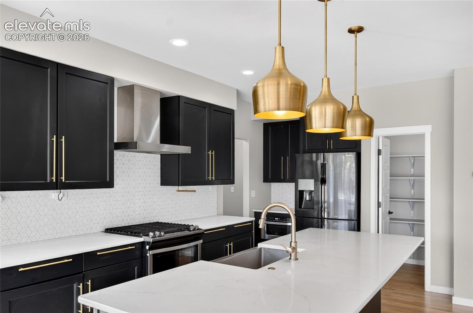 Kitchen featuring black cabinetry with gold-finish hardware, stainless steel appliances, and a white geometric tile backsplash