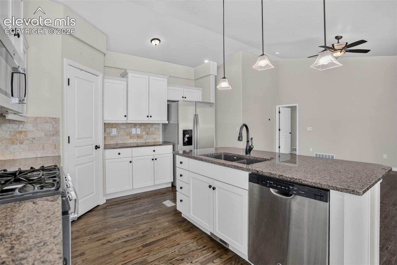 Kitchen featuring dark wood-finish flooring, white cabinetry, a stone-tiled backsplash, and a large island with a double basin sink and stainless steel dishwasher