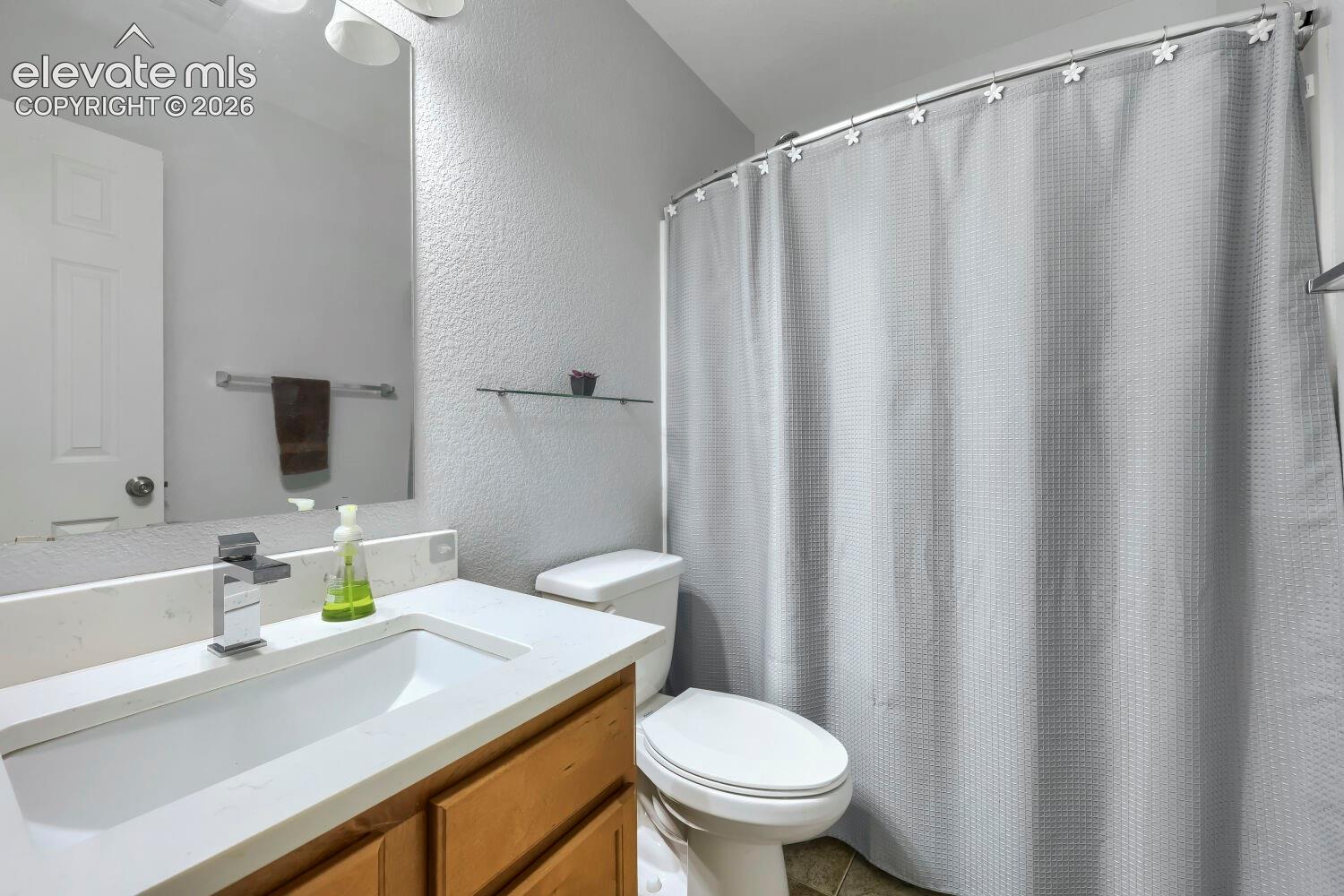 Bathroom featuring a wood-finish vanity with a stone-composite countertop, integrated rectangular sink, chrome single-handle faucet, and an oversized frameless mirror