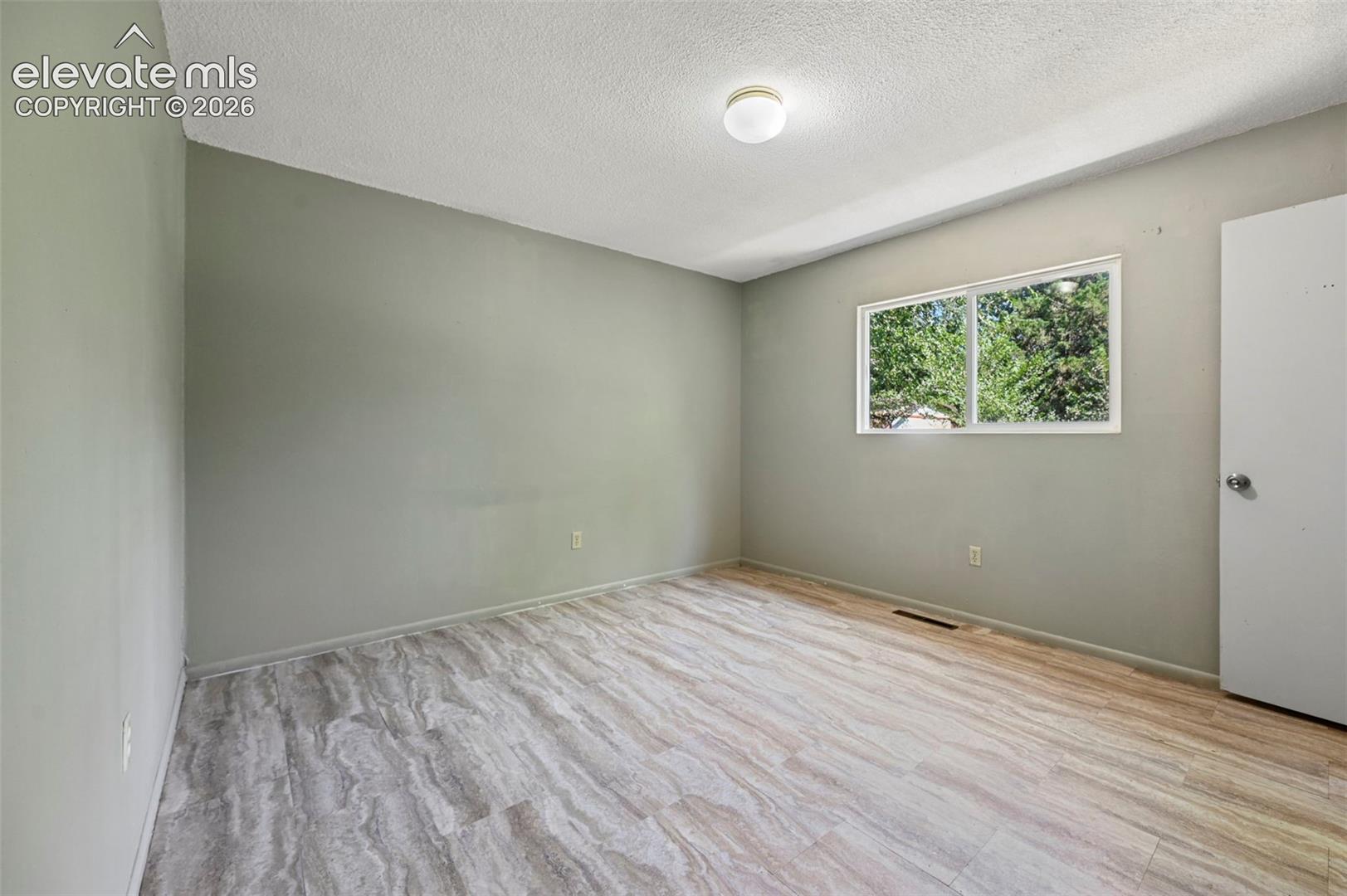 Interior room featuring wood-finish flooring, a double-pane window, neutral wall paint, and a ceiling-mounted light fixture
