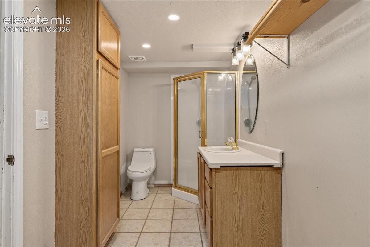 Bathroom in basement featuring a wood-finish vanity with an integrated sink, a corner shower enclosure, floor-to-ceiling built-in cabinetry, and ceramic tile flooring