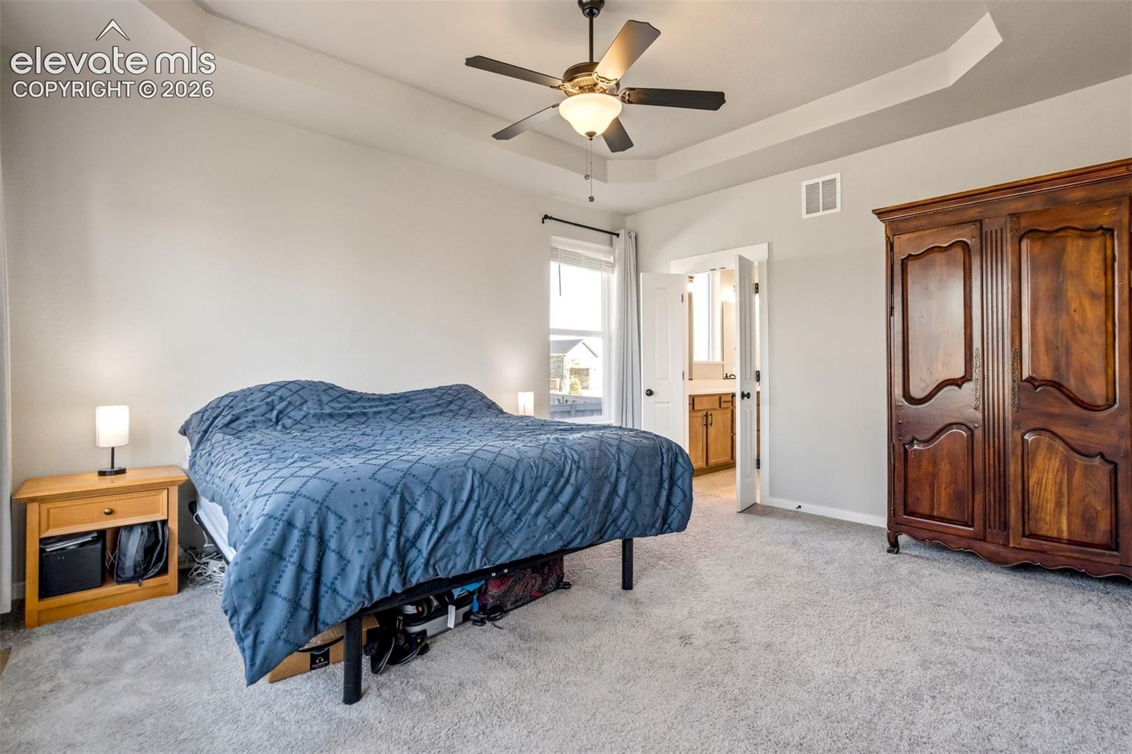 Bedroom featuring a tray ceiling, ceiling fan with integrated light fixture, carpeted flooring, and neutral wall tones