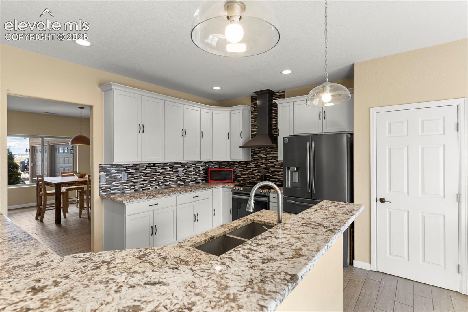 Kitchen featuring white cabinetry, stone-finish countertops, decorative tile backsplash, stainless steel appliances, and dual pendant lighting