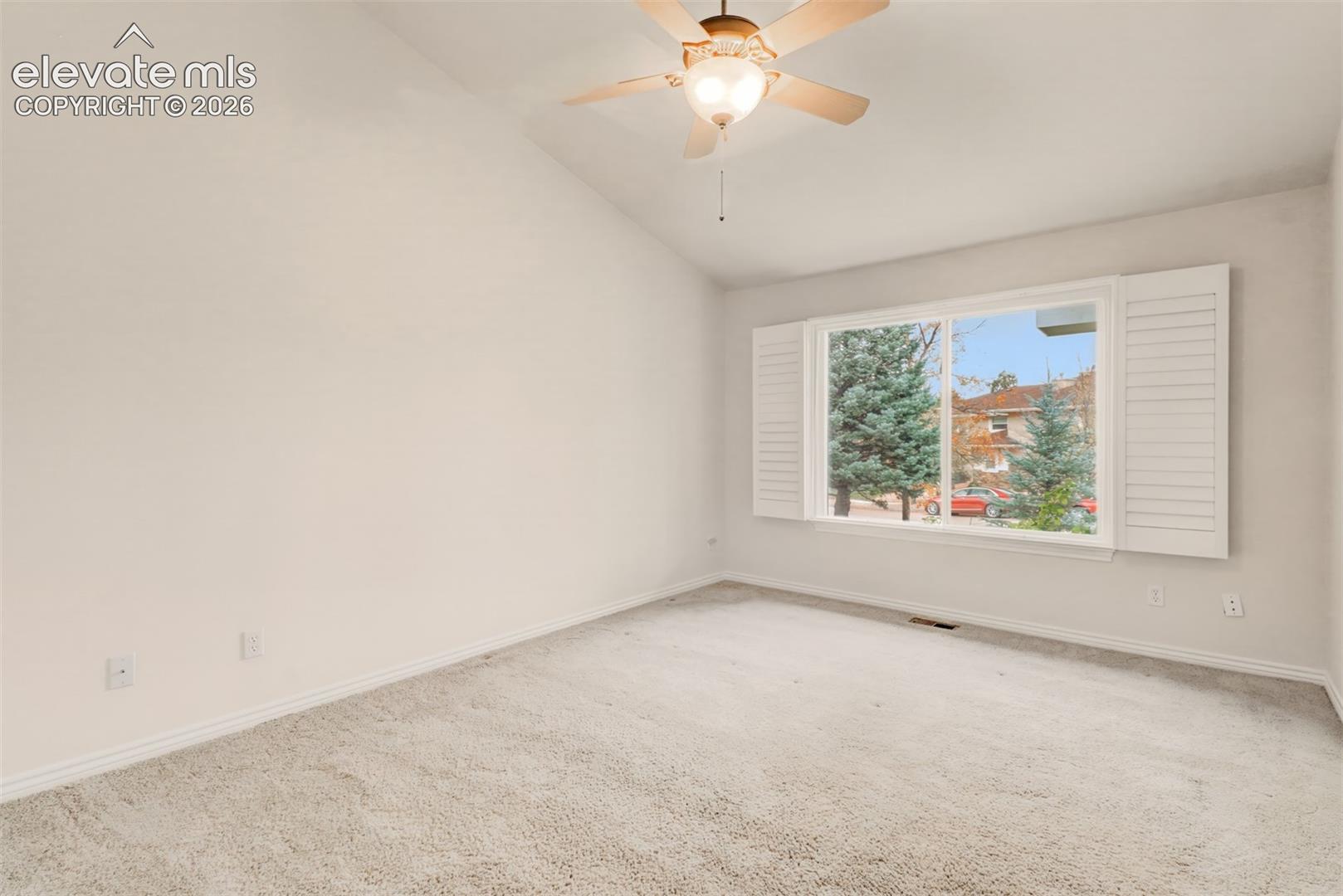 Main level guest bedroom, vaulted ceilings, large sliding window with plantation shutters, and ceiling-mounted light fixture with fan