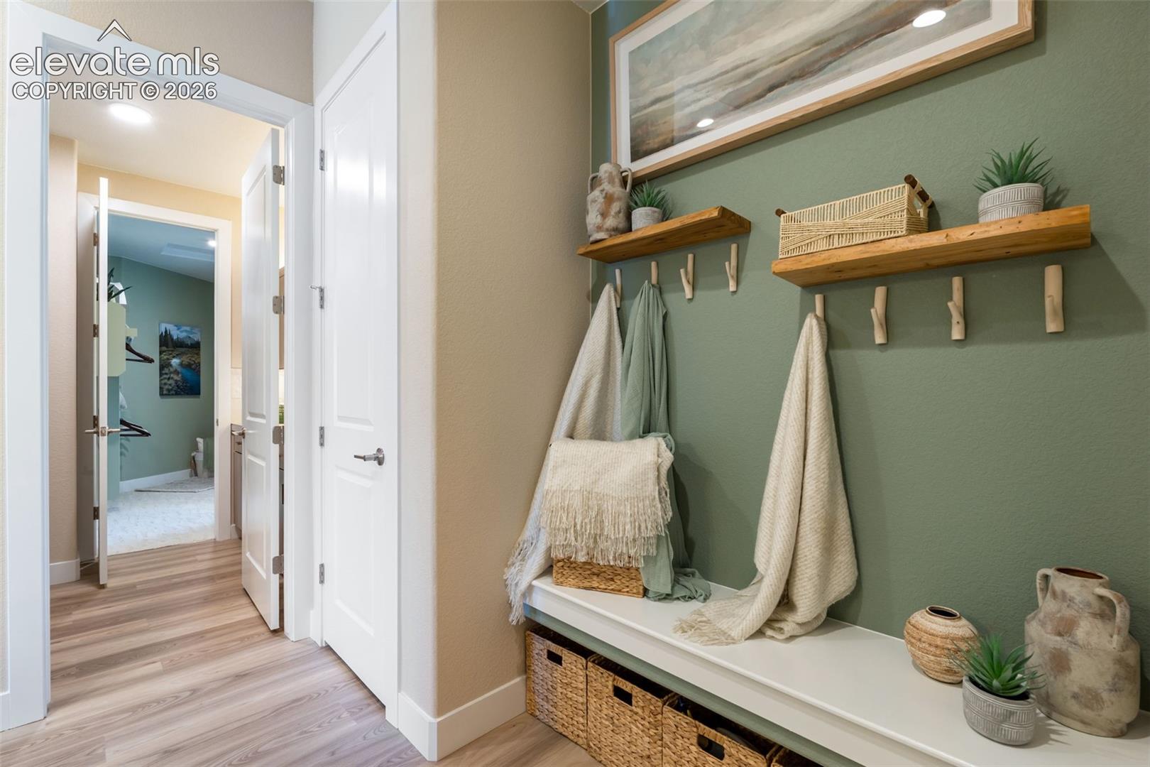 Built-in bench seating with storage, wall-mounted natural wood shelving, six integrated wall hooks, and wood-finish flooring