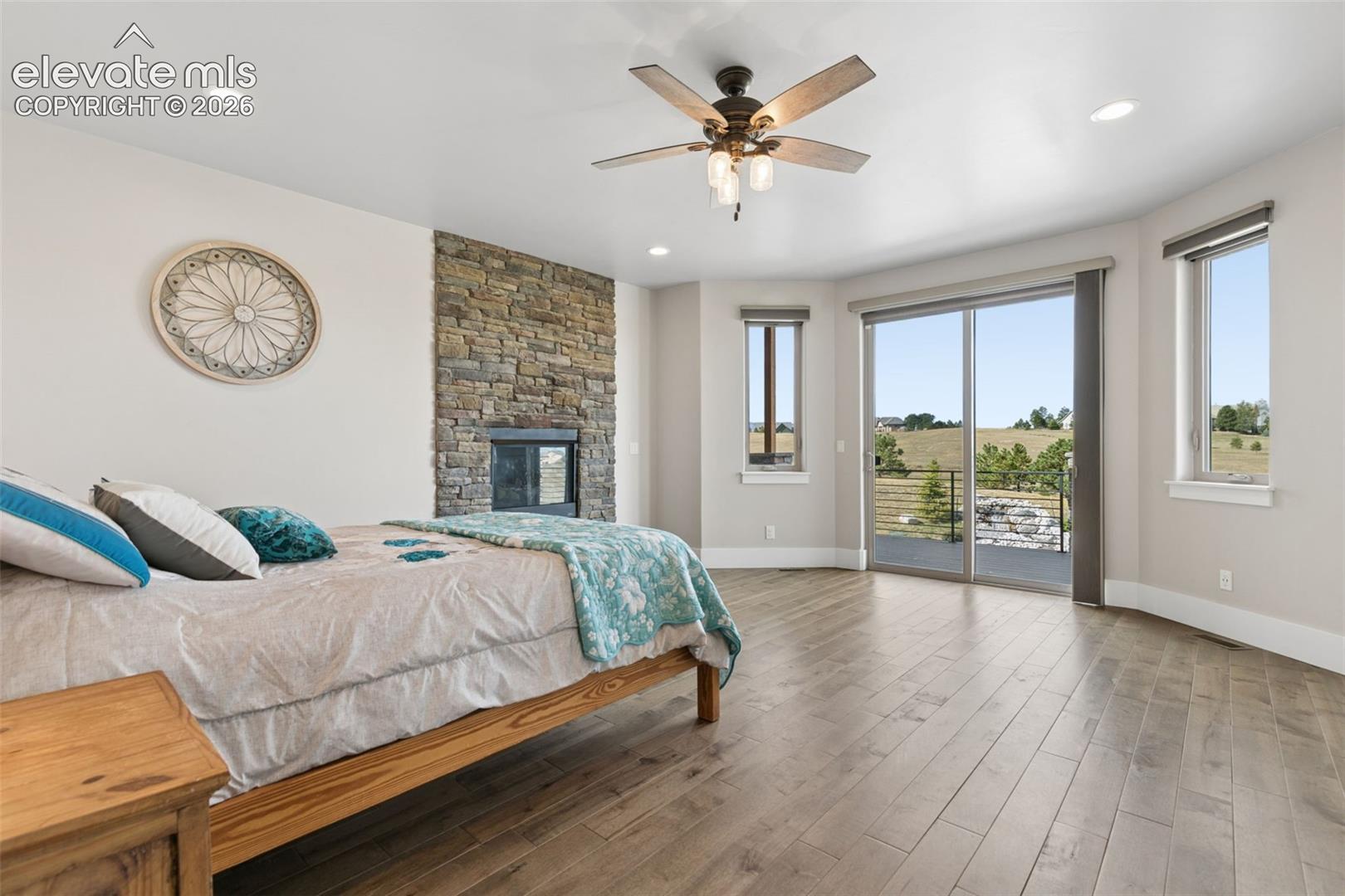 Stone-clad fireplace feature, recessed lighting, wood-finish flooring, ceiling fan, and sliding glass door to exterior