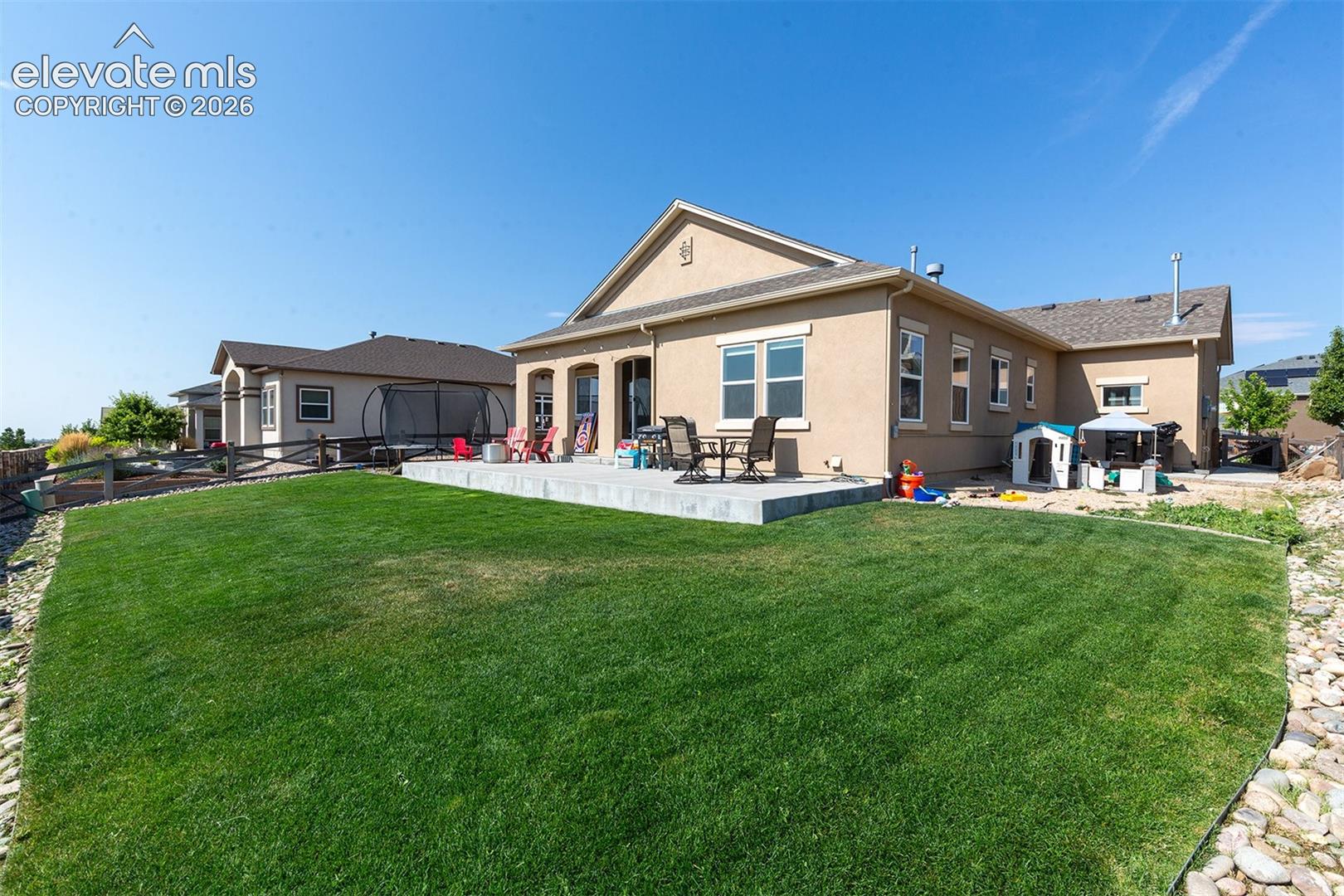 Expansive rear lawn with a level concrete patio, stucco exterior, and multi-pane windows
