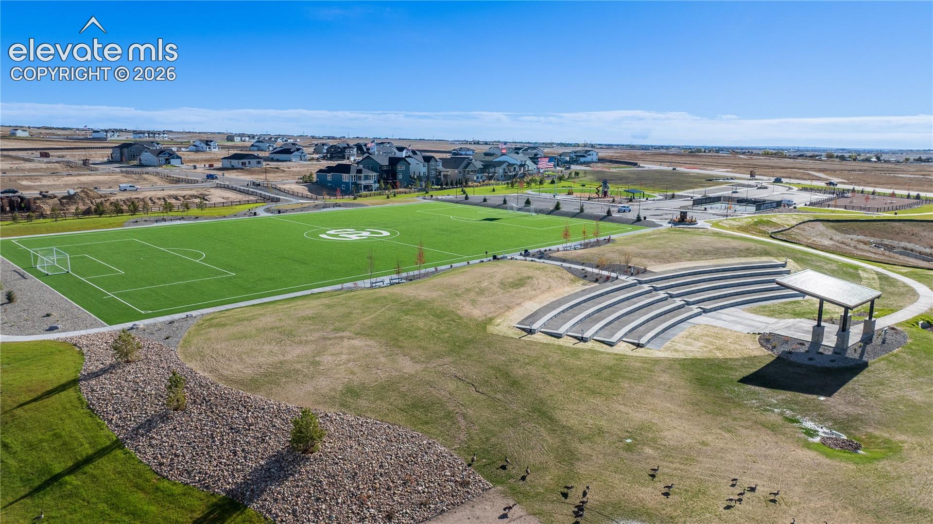 Recreational park area featuring a synthetic turf field, terraced concrete amphitheater seating, and a covered pavilion