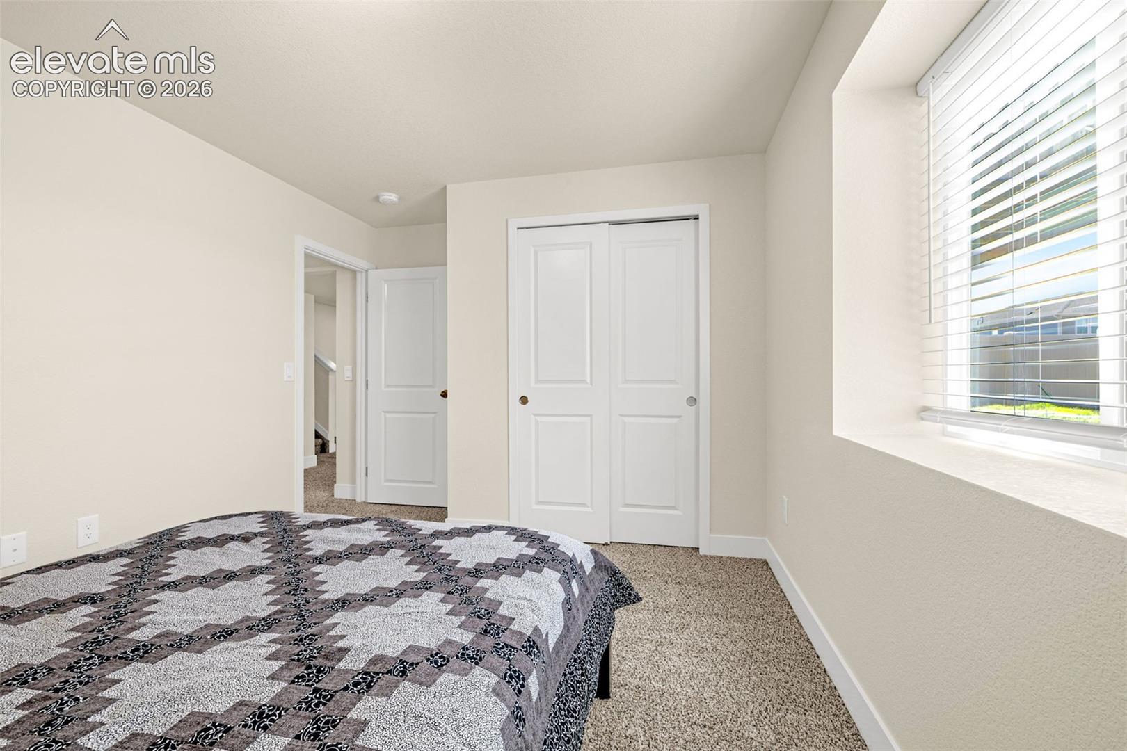Recessed window with blinds, bi-fold closet doors, and neutral carpeting