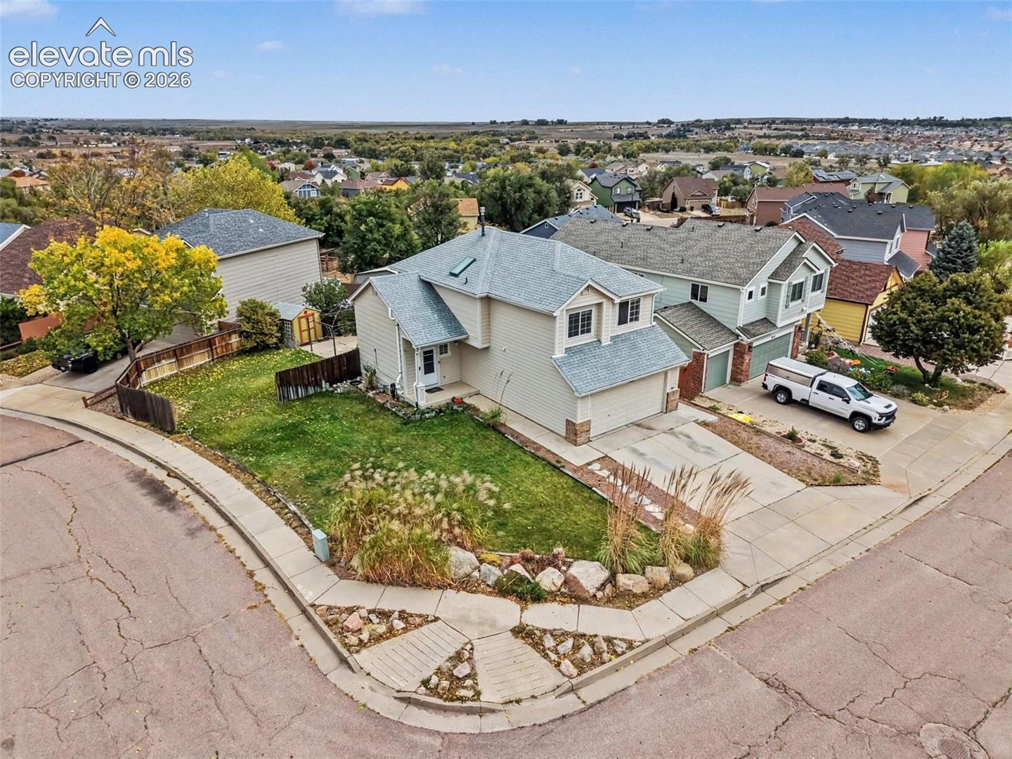 Corner lot residence featuring light-colored siding, a multi-gabled roofline with a skylight, an attached two-car garage, and landscaped front yard with stone accents