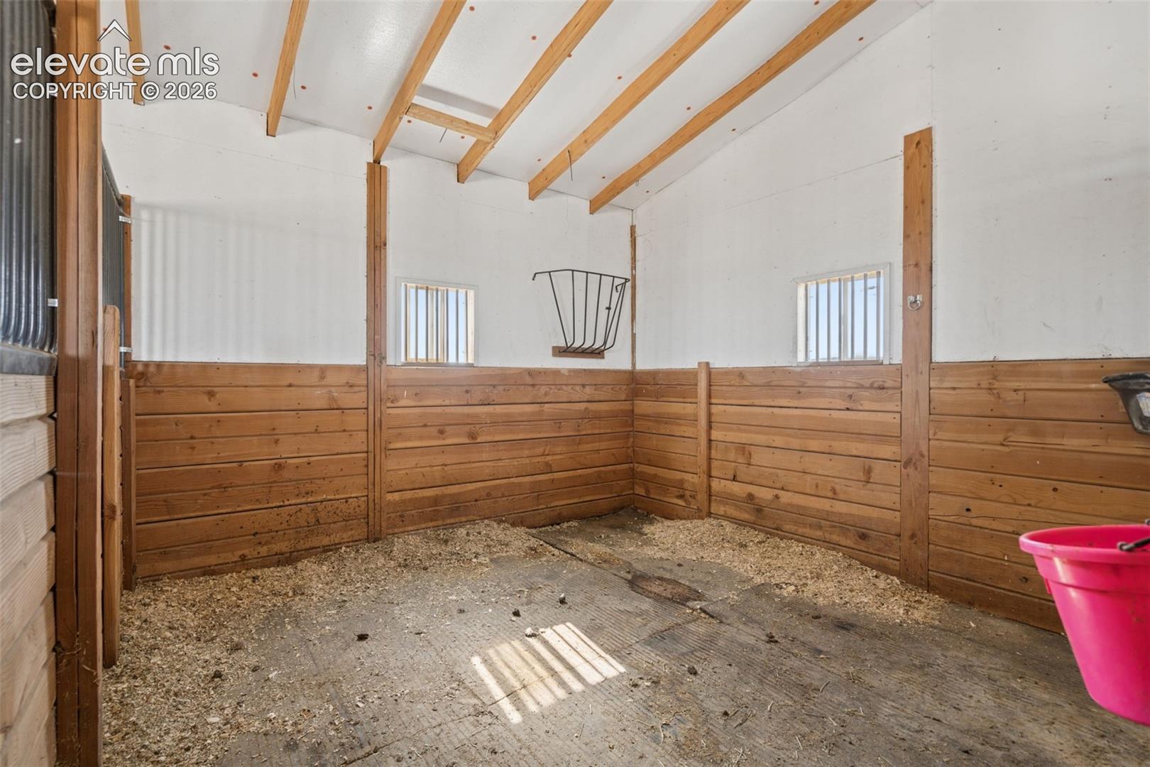 Stall featuring wood-plank walls, exposed ceiling rafters, barred windows, and a metal hay feeder