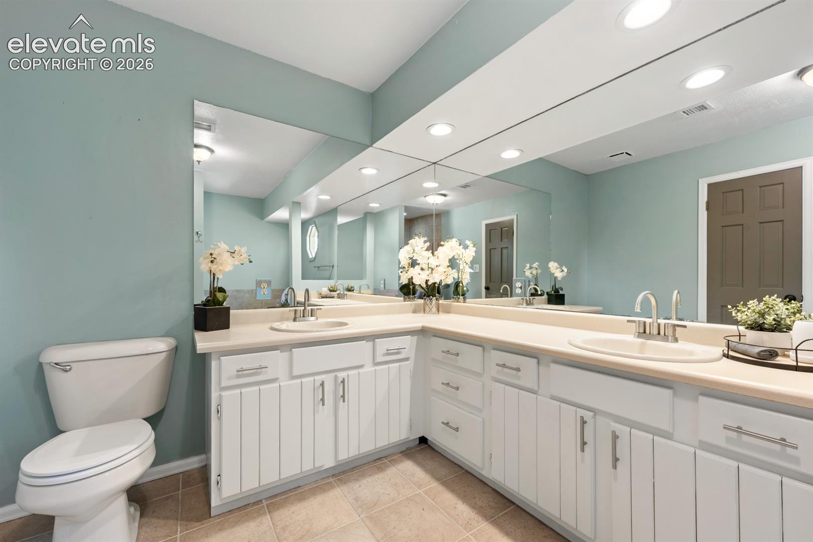 Dual vanity with integrated sinks, expansive wall-mounted mirror, recessed lighting, and tile flooring