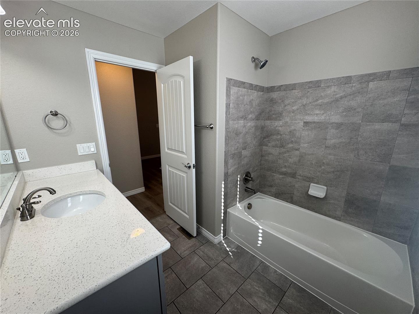 Bathroom featuring a white vanity with a speckled countertop, undermount sink, ceramic tile flooring, and a bathtub with stone-finish tile surround