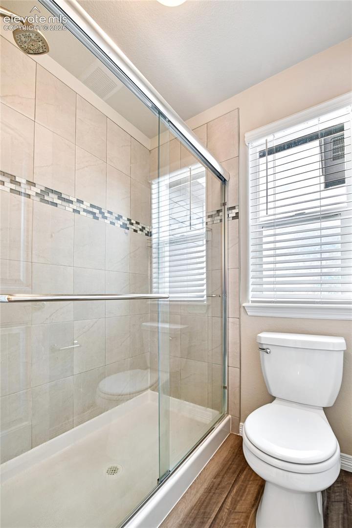 Walk-in shower featuring glass enclosure, ceramic tile surround with decorative mosaic inlay, integrated rain-style shower head, and wood-finish flooring